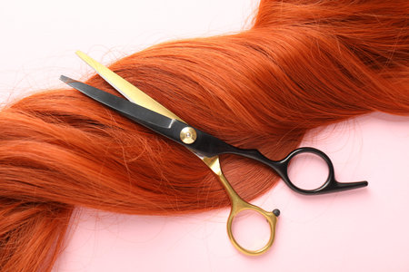 Hair strands and scissors on light pink background, top view