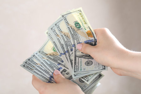 Woman counting dollar banknotes on beige background, closeup