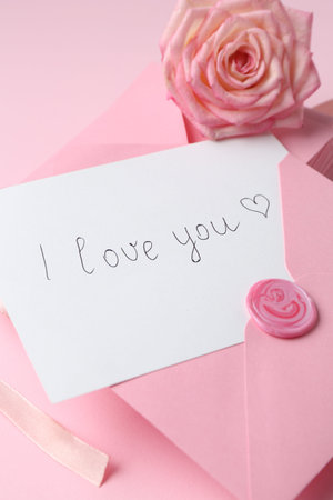 Stack of letters, card with phrase I Love You and rose flower on pink background, closeup