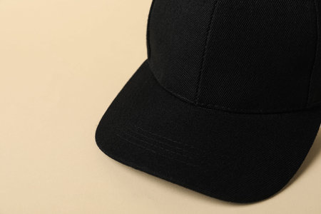 Black baseball hat on beige background, closeup. Space for text