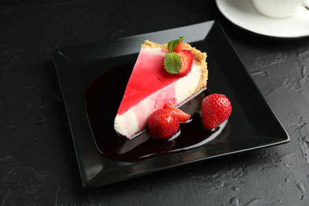 Piece of tasty cheesecake with strawberries, sauce and mint on black table, closeupの写真素材