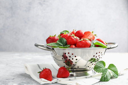Delicious ripe strawberries and green leaves on gray table, closeup. Space for textの写真素材