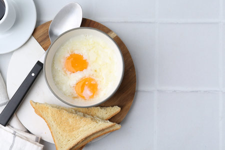 Traditional Asian breakfast with half-boiled eggs in bowl, coffee and toasted bread on white tiled...