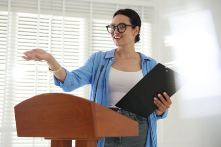 Woman giving public speech with microphone at lectern indoorsの写真素材