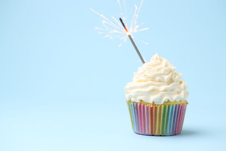 Burning sparkler in cupcake on light blue background, space for textの写真素材