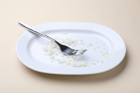 Dirty plate with rice and fork on beige background, closeupの写真素材