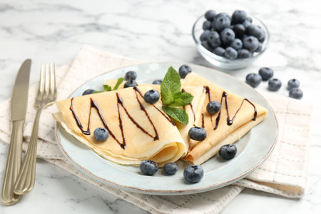 Tasty crepes with blueberries, chocolate sauce and mint served on white marble table, closeupの写真素材