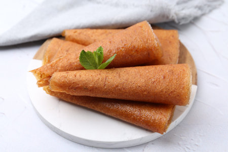 Delicious fruit leather rolls and mint on white table, closeup