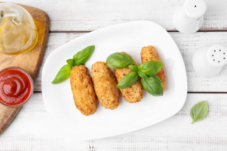 Tasty fried croquettes, basil and sauce on white wooden table, flat lay