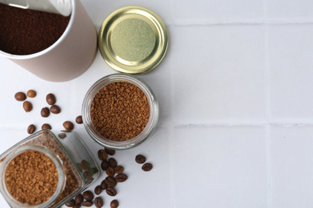 Instant coffee in jars and beans on white tiled table, flat lay. Space for textの写真素材