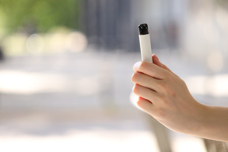 Young woman with electronic smoking device outdoors, closeup. Space for text