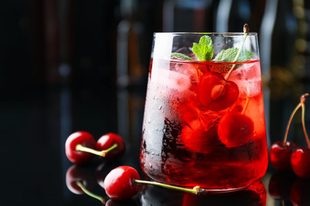 Tasty cherry soda water with ice cubes, berries and mint in glass on mirror table against blurred background, closeup. Space for textの写真素材