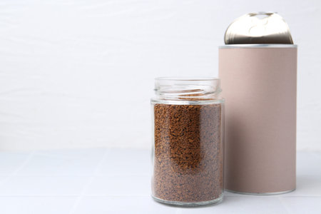 Instant coffee in jars on white tiled table, closeup. Space for text