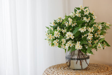 Beautiful jasmine flowers in vase on wicker table near window indoors, space for textの写真素材