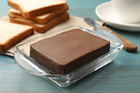 Block of tasty chocolate butter in glass keeper on light blue wooden table, closeup