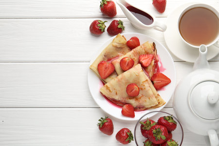 Delicious crepes with strawberries, sauce and tea on white wooden table, flat lay. Space for textの写真素材