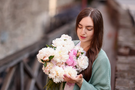 Charming woman with bouquet of beautiful peonies on city street. Space for textの写真素材