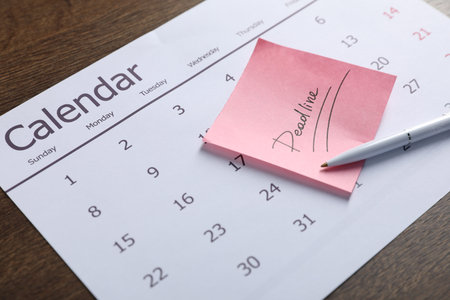 Sticky note with word Deadline, calendar and pen on wooden table, closeup