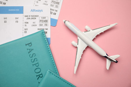 Passports with tickets and airplane model on pink background, flat lay