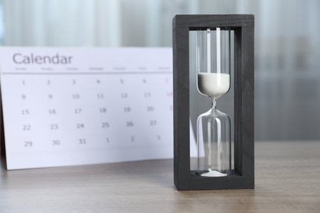 Deadline. Hourglass with flowing sand and calendar on wooden table indoorsの写真素材
