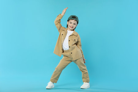 Happy little boy in baseball hat dancing on light blue backgroundの写真素材