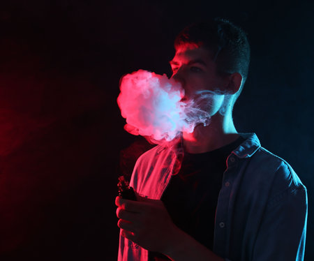 Man using electronic smoking device in neon lights on dark background, space for text