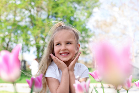 Cute little girl near beautiful pink tulips outdoorsの写真素材