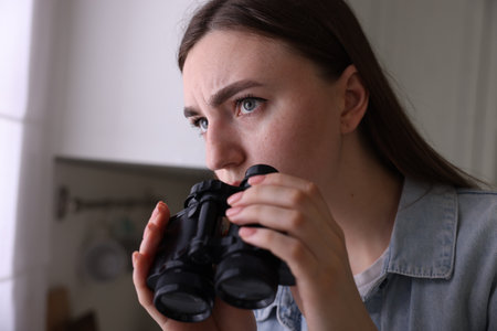 Paranoia. Worried woman with binoculars in kitchenの写真素材