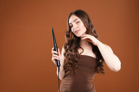 Woman curling her beautiful hair on brown background. Space for textの写真素材