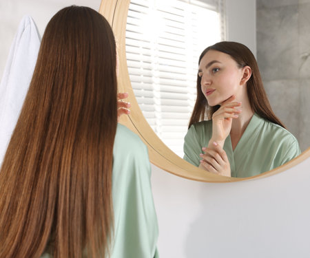 Beautiful woman looking at herself in mirror indoorsの写真素材