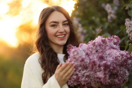 Portrait of smiling woman with lilac flowers outdoors in morningの写真素材