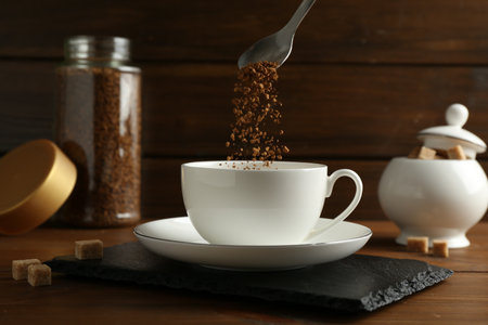 Putting granulated instant coffee into cup on wooden table, closeupの写真素材