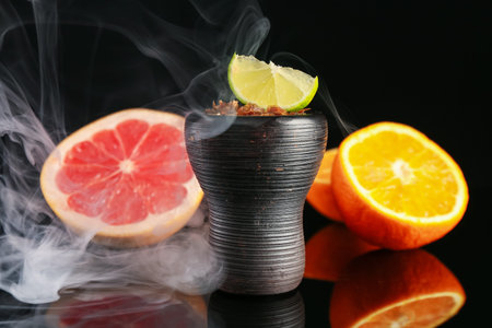 Hookah bowl with smoke and fruits on black table, closeup