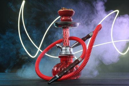 Hookah on wooden table with smoke in color lights against black backgroundの写真素材