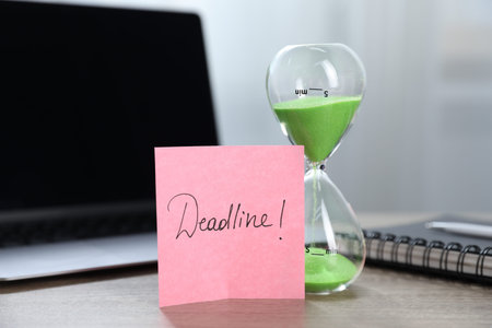 Sticky note with word Deadline, hourglass, notebook and laptop on wooden table indoors, closeup