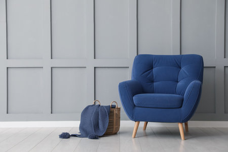 Comfortable blue armchair and basket with cloth near light gray wall indoors, space for textの写真素材