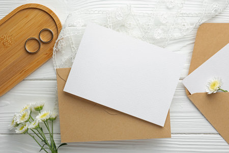 Wedding invitation cards, envelopes, silver rings, flowers and ribbon on white wooden table, flat layの写真素材