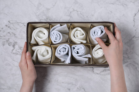 Woman putting white socks into organizer on light marble background, top view
