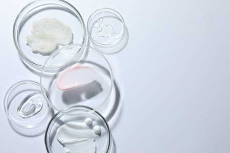 Different cosmetic products in Petri dishes on white background, flat lay. Space for text