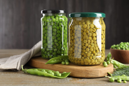 Pickled and fresh peas in jars, dill and pods on wooden table, closeupの写真素材