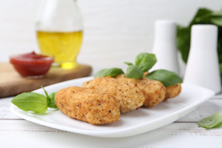 Tasty fried croquettes and basil on white wooden table, closeup