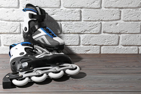 Pair of roller skates on wooden table near white brick wall, space for text