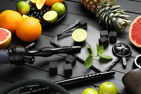 Hookah, coal and fresh fruits on black wooden table, closeup