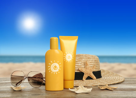 Sunscreen products, sunglasses and beach hat on wooden table near sea. Bottle and tube with drawings of sunの写真素材