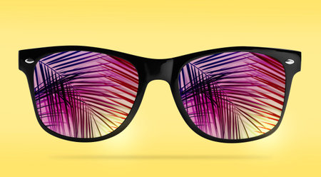 Bright sunglasses with reflection of palm on lenses against yellow gradient background