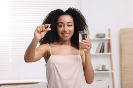 Beautiful Brazilian woman with glass of water and collagen pill indoors, selective focusの写真素材