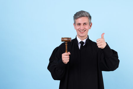 Smiling judge with mallet showing thumbs up on light blue background. Space for textの写真素材