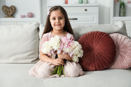 Cute little girl with bouquet of beautiful peonies on sofa at homeの写真素材