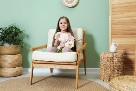 Cute little girl with bouquet of beautiful peonies in armchair near green wall indoorsの写真素材