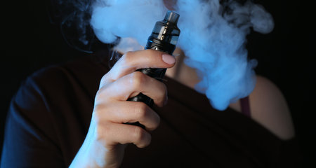 Woman using electronic smoking device in neon lights on black background, closeup